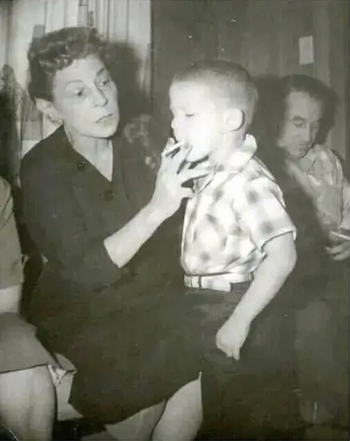 AI Restored Your Photo But It Looks Wrong? We Fix AI Restoration Mistakes 1 Damaged original black and white photo of a woman holding a cigarette to a young boy’s lips, with a man and another relative beside them